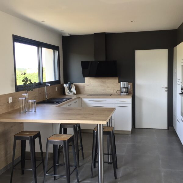 Résliation d'une cuisine intemporelle aux facades blanches et plan de travail coloris bois, avec une table à hauteur dans le prolongement du plan de travail.