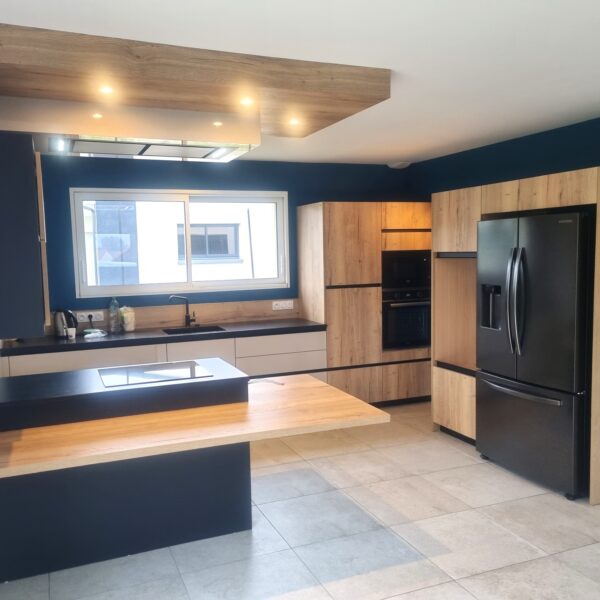 Réalisation d'une cusine en ton bois, blanc et noir, intégration d'une partie repas dans l'ilot, intégration d'une hotte de plafond dans un coffrage assortis à la cuisine. Projet sur Bressuire.